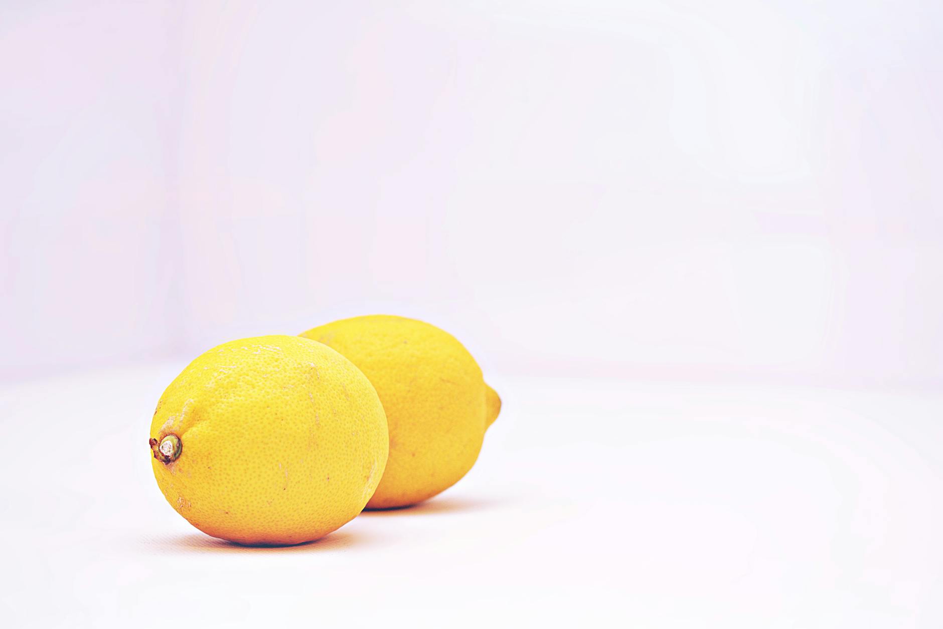 Two vibrant lemons placed against a minimalistic white background, symbolizing freshness and sensory reconnection.