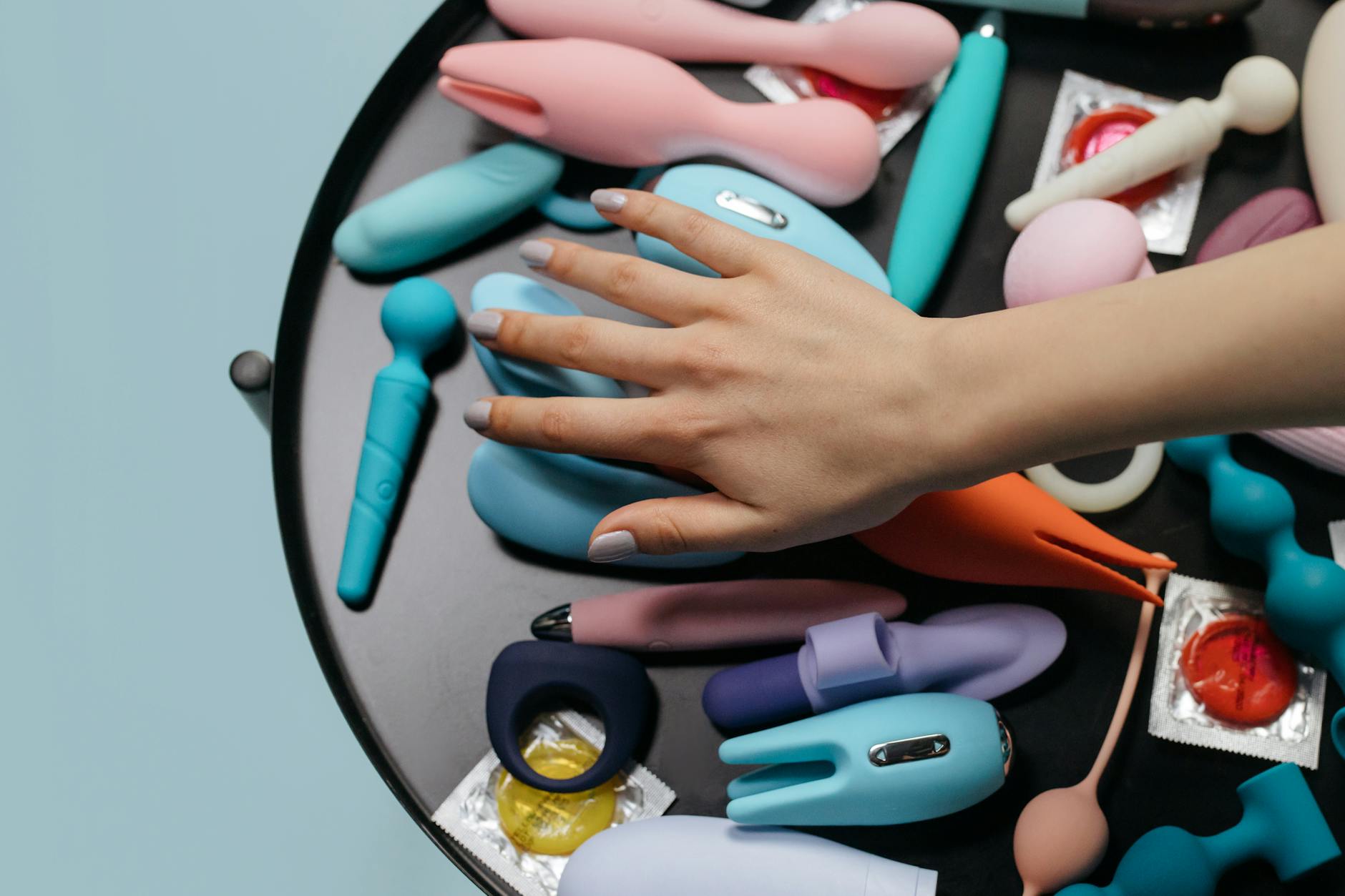 A hand reaching over a variety of colorful lemon vibrators and sex toys arranged on a table.