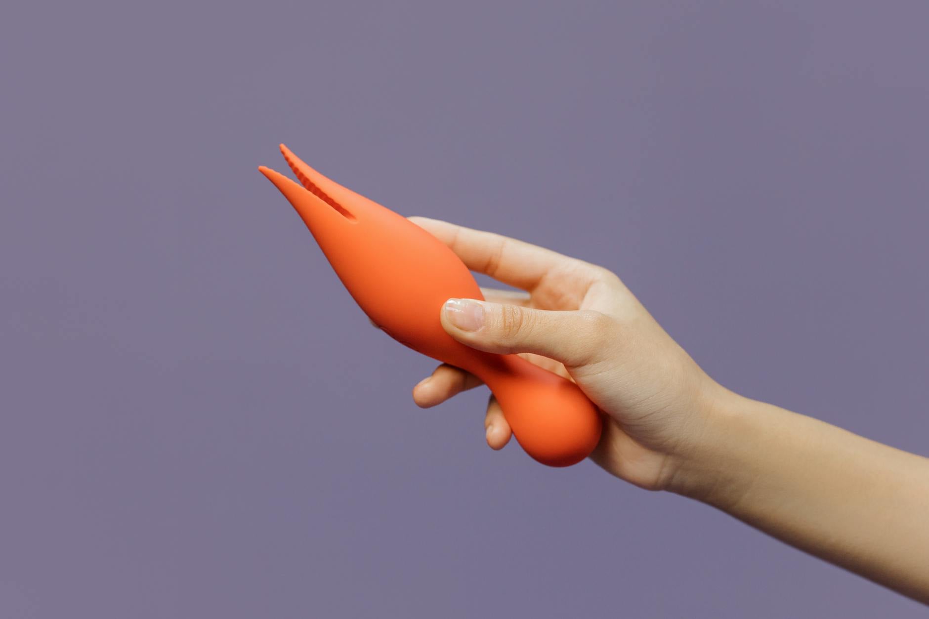 A hand holding a lemon-colored vibrator against a minimalist purple backdrop, representing reclaiming pleasure.
